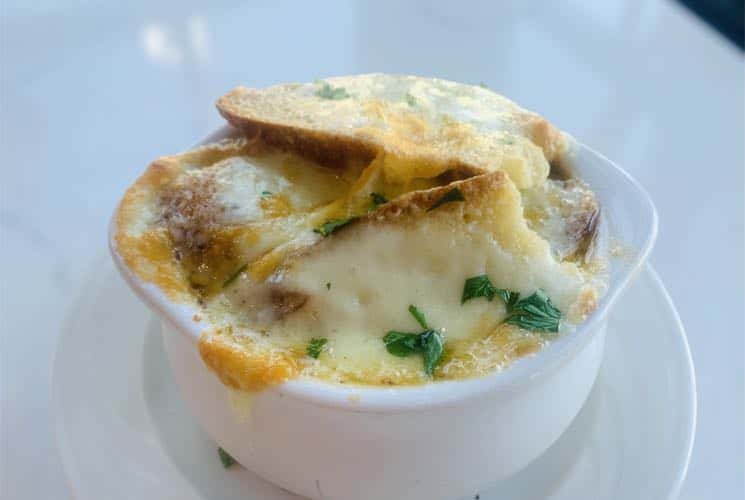 Close up view of baked onion soup in white bowl