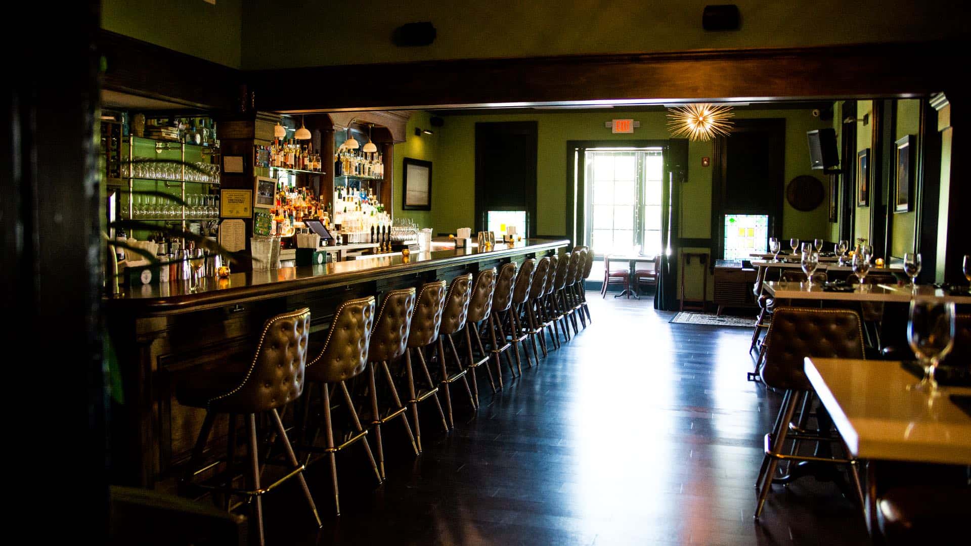 Bar and dining area with green walls, dark green trim, hardwood flooring, white tables, and tall bar stool leather chairs