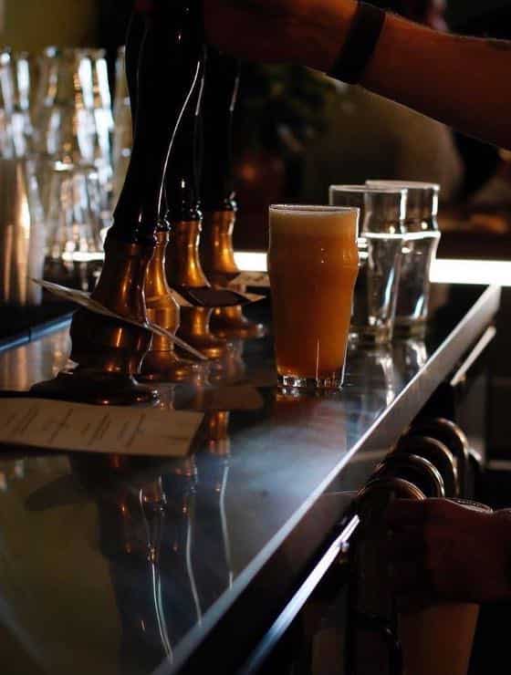 Close up view of beer in a tall glass on stainless steel counter near tap